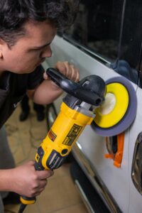 Leistungen Close-up of a man using a power polisher on a car in a workshop setting for auto detailing.