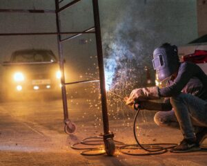 Leistungen A welder at work with sparks flying in an industrial setting during night time.