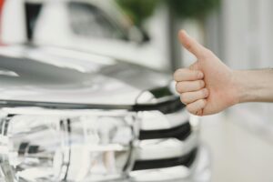 Leistungen Close-up of a thumbs up gesture next to a car headlight, symbolizing approval or satisfaction.