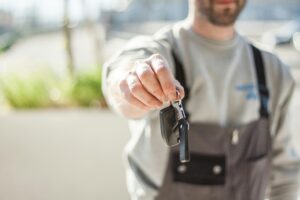 Leistungen Hand holding a car key outdoors, blurred background, shallow focus.